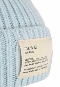 Light blue knitted beanie with a ribbed texture. A woven label on the side features the word "thank-ful" and related synonyms.