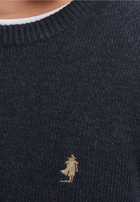 Ciemnoniebieski sweter dziany o prążkowanej fakturze z małą złotą haftowaną postacią po lewej stronie. Okrągły dekolt, casualowy design.