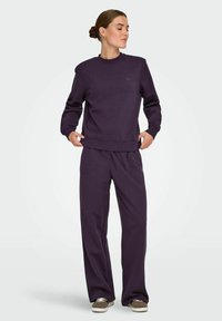 Lilla sweatshirt og matchende joggers i et blødt stof. Toppen har en rund hals og ribbede mansjetter, mens bukserne har en afslappet pasform.