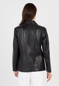 Zwarte leren blazer met een getailleerde pasvorm. Bevat een gelapte kraag, lange mouwen en een gladde textuur met minimale stikseldetails.