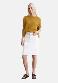 Haut en tricot moutarde à manches courtes, associé à une jupe midi en denim blanche avec des poches avant et arrière, complété par des sandales noires.