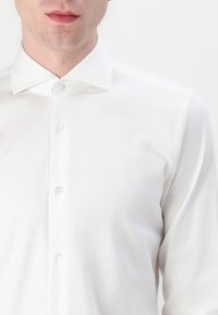Weißes Langarm-Hemd mit Knöpfen, aus glattem Stoff. Verfügt über einen klassischen Kragen und fünf klare Kunststoffknöpfe entlang der Knopfleiste.