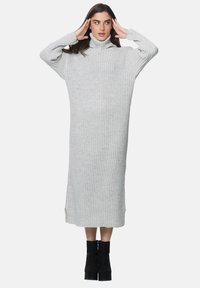 Jasnoszara, prążkowana sukienka swetrowa z wysokim kołnierzem, długimi rękawami i bocznymi rozcięciami, zestawiona z czarnymi botkami do kostek.