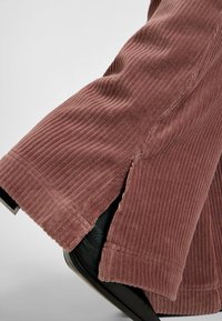 Pantaloni in velluto a coste di colore rosa polveroso, con righe verticali, una forma leggermente svasata e un dettaglio con spacco laterale all'orlo.