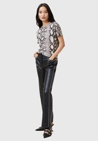 Schlangenprint top met korte mouwen, gecombineerd met hoogtaille zwarte leren broeken met studs langs de zijkant. Zwarte hakken.