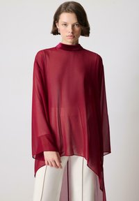 Przezroczysta burgundowa tunika z wysokim kołnierzem, długimi rękawami i luźnym krojem. Materiał ma gładką fakturę, z wysokimi rozcięciami po bokach.