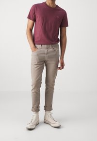 Mörkröd bomulls-T-shirt med en liten röd logotyp, tillsammans med ljusbeige tapered jeans och vita höghalkiga stövlar med texturerade sulor.