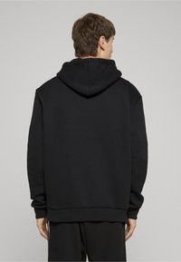 Sweat-shirt à capuche noir avec une coupe décontractée, doté d'une poche kangourou et de poignets côtelés. Tissu lisse et détails minimalistes à l'arrière.