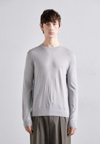 Pull long gris clair à manches longues avec un col rond, coupe ajustée, texture douce et poignets côtelés, associé à un pantalon gris plissé.