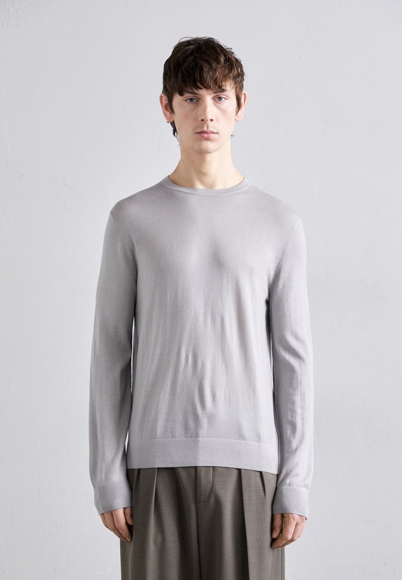Pull long gris clair à manches longues avec un col rond, coupe ajustée, texture douce et poignets côtelés, associé à un pantalon gris plissé.