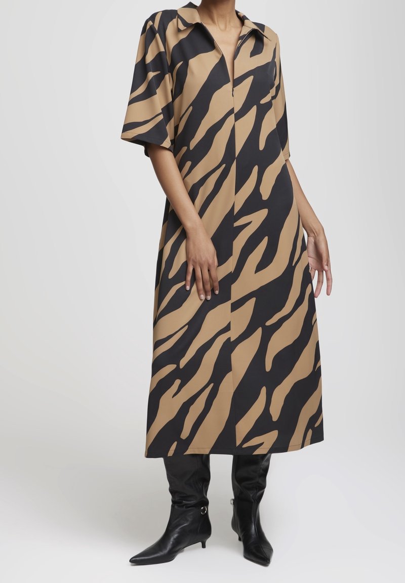 Personne portant une robe imprimé zèbre beige et noire longueur genou, manches courtes, et des bottines noires pointues à talons.