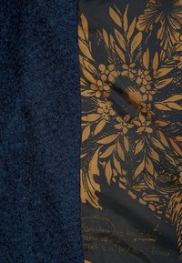 Tessuto testurizzato blu navy a sinistra, abbinato a un materiale nero liscio con un motivo floreale dorato e testo scritto a mano a destra.