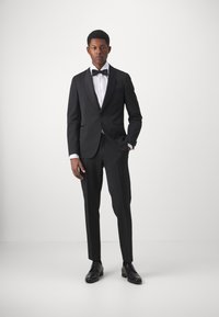 Sort smoking med satin revers, hvid skjorte og sort butterfly. Slim-fit bukser og sorte dresssko. Glat, skræddersyet stof.