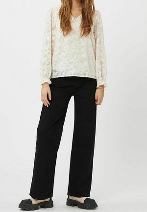 Witte bloemenkantblouse met lange mouwen, gecombineerd met zwarte wijde broekspijpen en zwarte platformsandalen. Gestructureerde, gelaagde uitstraling.