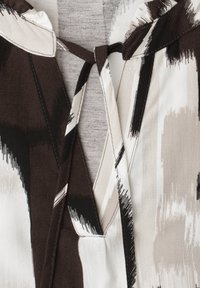 Close-up of fabric with abstract black, white, and gray brushstroke pattern and overlapping sewn panels or straps.