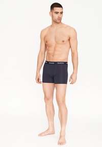 Boxers azul marino hechos de suave algodón con un ajuste ceñido, con una cinturilla elástica negra que tiene texto en blanco con el logo.