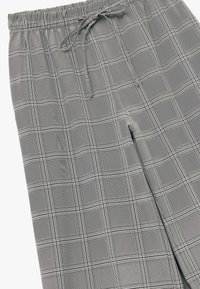 Grijze geruite loungebroek met een elastische tailleband, koord en een zachte textuur. Heeft zwarte ruitpatronen en een ontspannen pasvorm.
