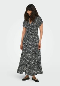 Zwarte maxi-jurk met korte, gerimpelde mouwen, voorzien van een v-hals en een split aan de voorkant, bedrukt met kleine witte en blauwe bloemen.
