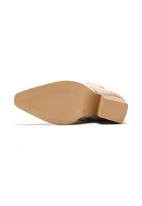 Zapato de tacón beige con parte superior texturizada y perforaciones. Presenta un tacón grueso y una suela de goma lisa y plana, que proporciona estabilidad.
