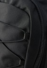 Κοντινό πλάνο μαύρου σακιδίου πλάτης, κατασκευασμένο από υφασμάτινη υφή. Διαθέτει ελαστικούς ιμάντες, επενδυμένη πλάτη και έντονη αντίθετη ραφή.