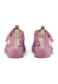 Rosa Lederkinderschuhe mit einem Klettverschluss, strukturierten Akzenten und einer sandfarbenen Schlaufe. Mit einem Bärenemblem und Gummisohle.
