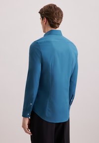 Teal shirt met lange mouwen, een frisse kraag, knoopmanchetten en een gladde textuur. Heeft een getailleerde pasvorm en een gebogen zoom aan de achterkant.