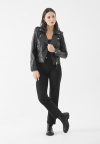 Giacca da motociclista in pelle nera con cerniere e accessori in argento, abbinata a un top fitted nero e pantaloni dritti neri, completata con stivali neri chunky.