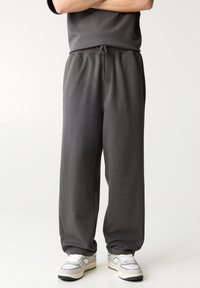 Donkergrijze, lichte loungebroek met elastische tailleband en trekkoord. Rechtaflopende pijpen, zachte textuur, minimalistische stijl.