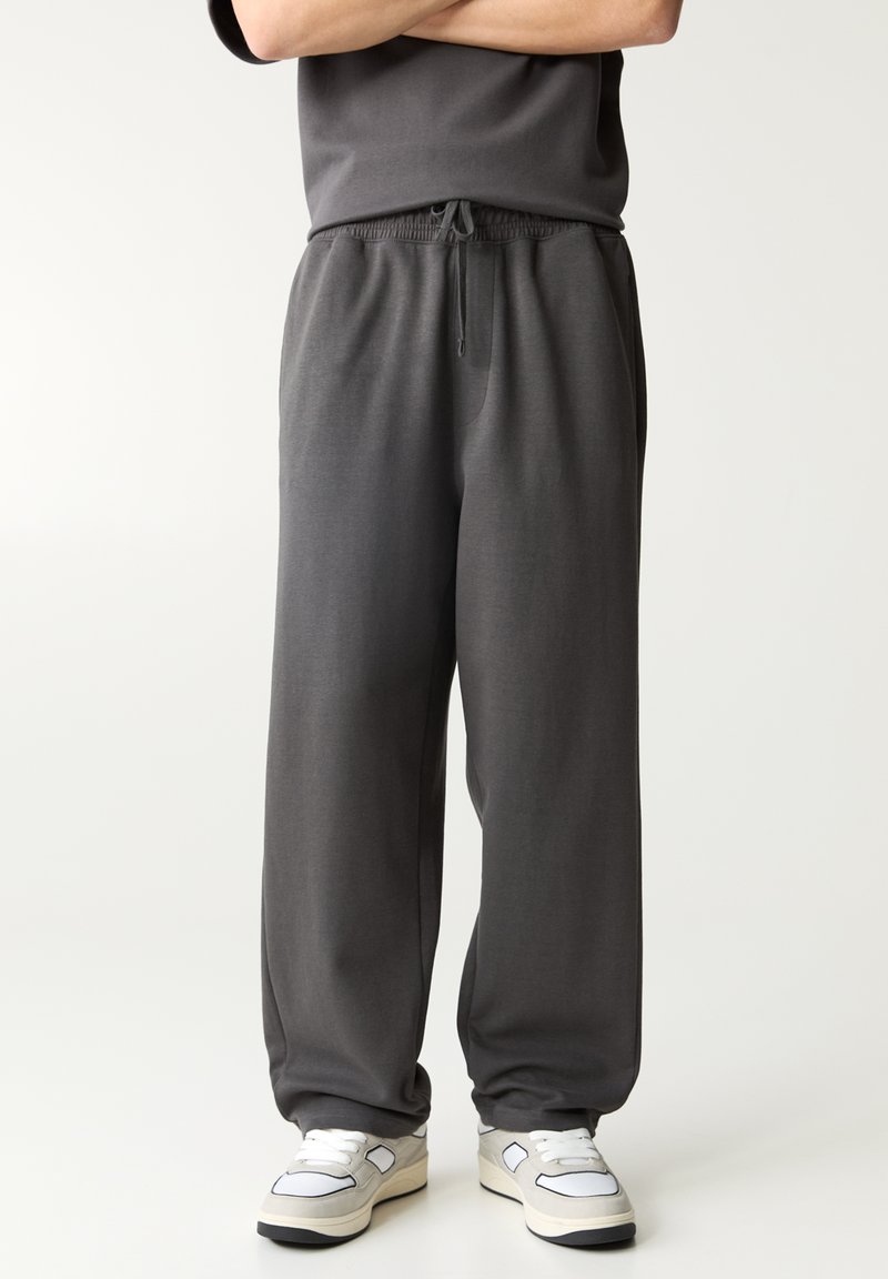 Donkergrijze, lichte loungebroek met elastische tailleband en trekkoord. Rechtaflopende pijpen, zachte textuur, minimalistische stijl.