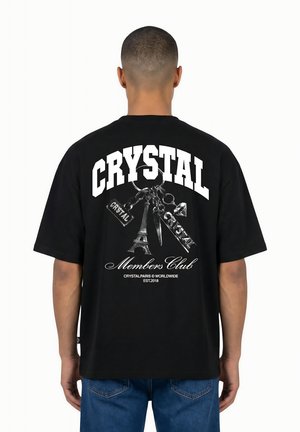 Homme portant un t-shirt noir avec texte blanc « CRYSTAL » et un graphisme porte-clé incluant la Tour Eiffel et « Members Club » dans le dos.