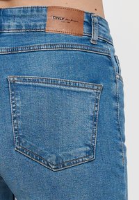 Blaue Denim-Jeans verfügen über eine Gesäßtasche und ein braunes Lederlabel mit der "ONLY"-Marke. Der Stoff hat eine glatte Textur und leichte Verwaschungen.