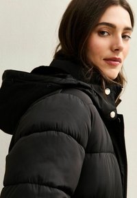 Czarna puchowa kurtka z kapturem, z zamkiem błyskawicznym i zatrzaskami, pikowana tekstura oraz gładkie wykończenie.