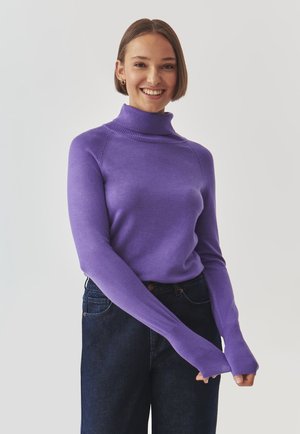 Pull encolure bateau violet à manches longues avec un col côtelé, assorti à un jean en denim foncé, présentant une coupe ajustée et une texture lisse.