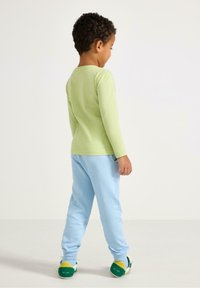 Grünes Langarmshirt und hellblaue Jogginghose, kombiniert mit grünen und gelben Turnschuhen, von hinten betrachtet. Schlichtes Design und bequemer Sitz.
