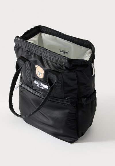 Μαύρη τσάντα tote Moschino Baby με λογότυπο αρκουδάκι, διπλές λαβές, μπροστινή τσέπη με φερμουάρ και ανοιχτό πάνω μέρος που δείχνει το ανοιχτό εσωτερικό ύφασμα.