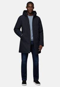 Navy padded coat with a hood, featuring a zip and snap closure, paired with a light blue sweater and dark jeans, complete with black sneakers.