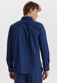 Marineblå skjorte med vertikale blå striber, knapmanchetter og spidse kraver. Glat stof med en skræddersyet pasform og rygplysdetail.