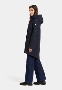 Marinfärgad vattentät jacka med huva, sidofickor och tryckknappar. Designad i en avslappnad passform, kombinerad med vida jeans och svarta stövlar.