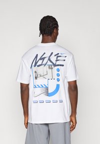 Λευκό μπλουζάκι Nike με γραφικό σχέδιο που διαθέτει μπλε και γκρι λεπτομέρειες, συμπεριλαμβανομένης μιας εικόνας μπάσκετ και αφηρημένων σχημάτων στην πλάτη.