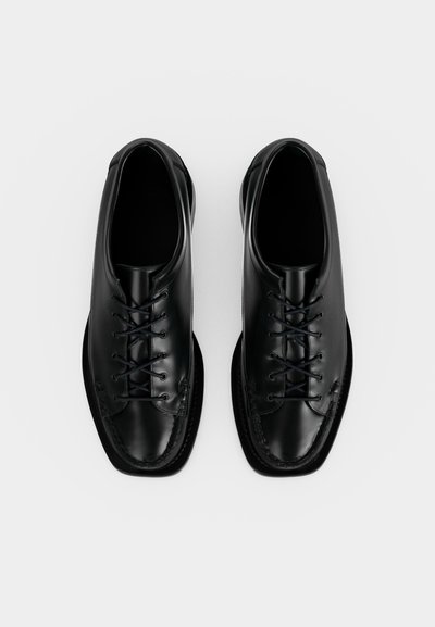 Paire de chaussures habillées en cuir noir à lacets, bouts carrés, vues de dessus sur un fond blanc uni.