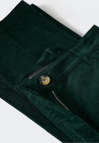 Tumma vihreät samettihousut nappisuljennalla, vetoketjulla ja siisteillä ommelyksillä. Rakenteellinen kangas, jossa näkyvä uurteinen kuvio.