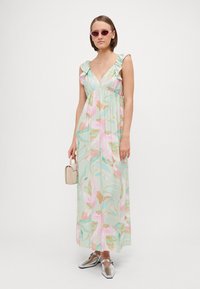 Maxi φόρεμα σε μαλακό ύφασμα με παστέλ floral σχέδιο, με ρυάκια τιράντες, βαθύ V-λαιμό και ελαστική μέση. Συνδυασμένο με ασημένια παπούτσια και μια μικρή τσάντα.