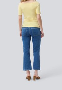 Gul, off-shoulder tætsiddende top parret med blå, flagrende jeans. Jeansene har et klassisk fem-lomme design og en medium vask. Brune blokhæle.