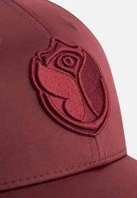 Rode baseballpet met een gladde stoftextuur, voorzien van een geborduurd rozenembleem in een vergelijkbare tint. Gebogen klep met zichtbare stitching.