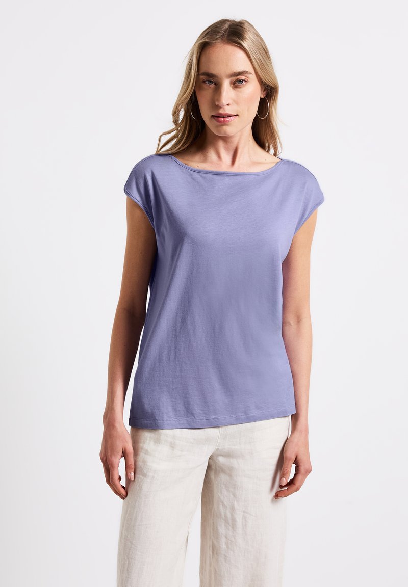 Top corto viola chiaro a maniche corte con una scollatura ampia e una texture liscia e morbida, abbinato a pantaloni di lino leggeri e morbidi.