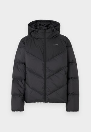 Chaqueta tipo puff negra con cierre de cremallera y capucha. Patrón de chevrón en el cuerpo, con un pequeño logo blanco en el pecho. Textura suave.
