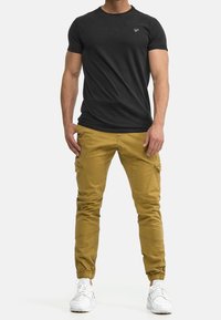 T-shirt noir à manches courtes avec un col rond, associée à un pantalon cargo kaki doté de multiples poches et de bas resserrés, porté avec des baskets blanches.