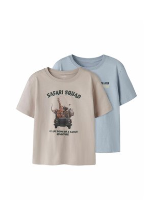 Dos camisetas de manga corta para niños, beige con estampado de animales de safari y azul con texto amarillo parcial en la parte delantera, fondo liso.