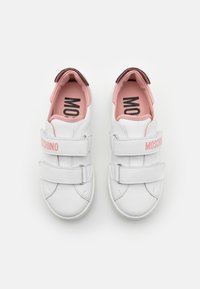 Zapatillas de piel blanca con acentos en rosa. Cuentan con correas de velcro y un logo de la marca en el lateral. Textura suave y diseño de puntera redondeada.