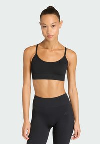 Μαύρο αθλητικό σουτιέν με λεπτές τιράντες, φαρδιά ζώνη και λείο υλικό; συνδυάζεται με ψηλόμεσα μαύρα κολάν που διαθέτουν μια διακριτική επωνυμία.